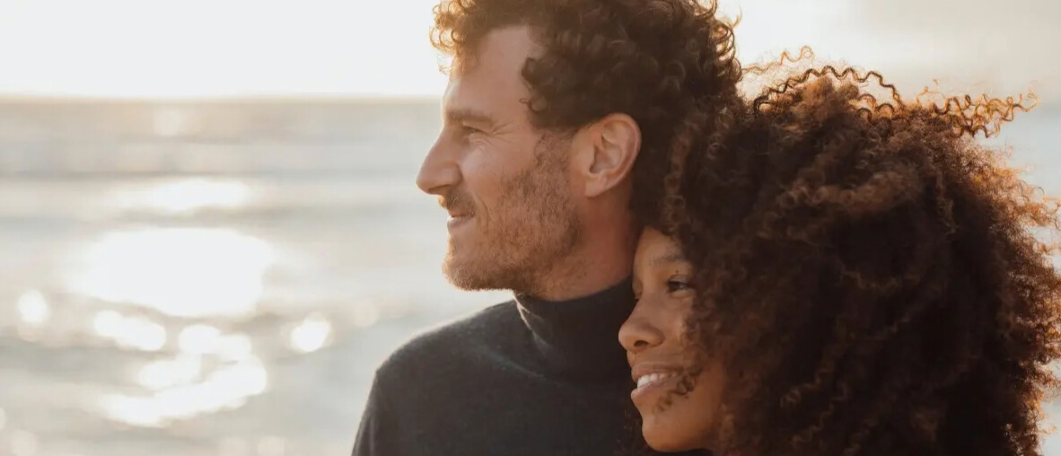 Couple side by side looking in the distance with the sea in the back.