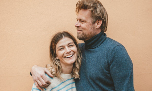 Couple laughing together in front of an orange wall. Couple laughing together in front of an orange wall.